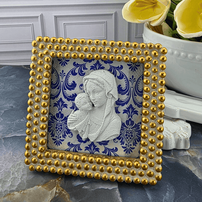 A square decorative picture frame with a gold beaded border and a white relief sculpture of the Virgin Mary holding baby Jesus, set against a blue and white damask pattern. Sister Dulce Gift Shop, Shepherds Staff, Religious Store, Cypress Springs Mercedarian Prayer Center, Catholic, 