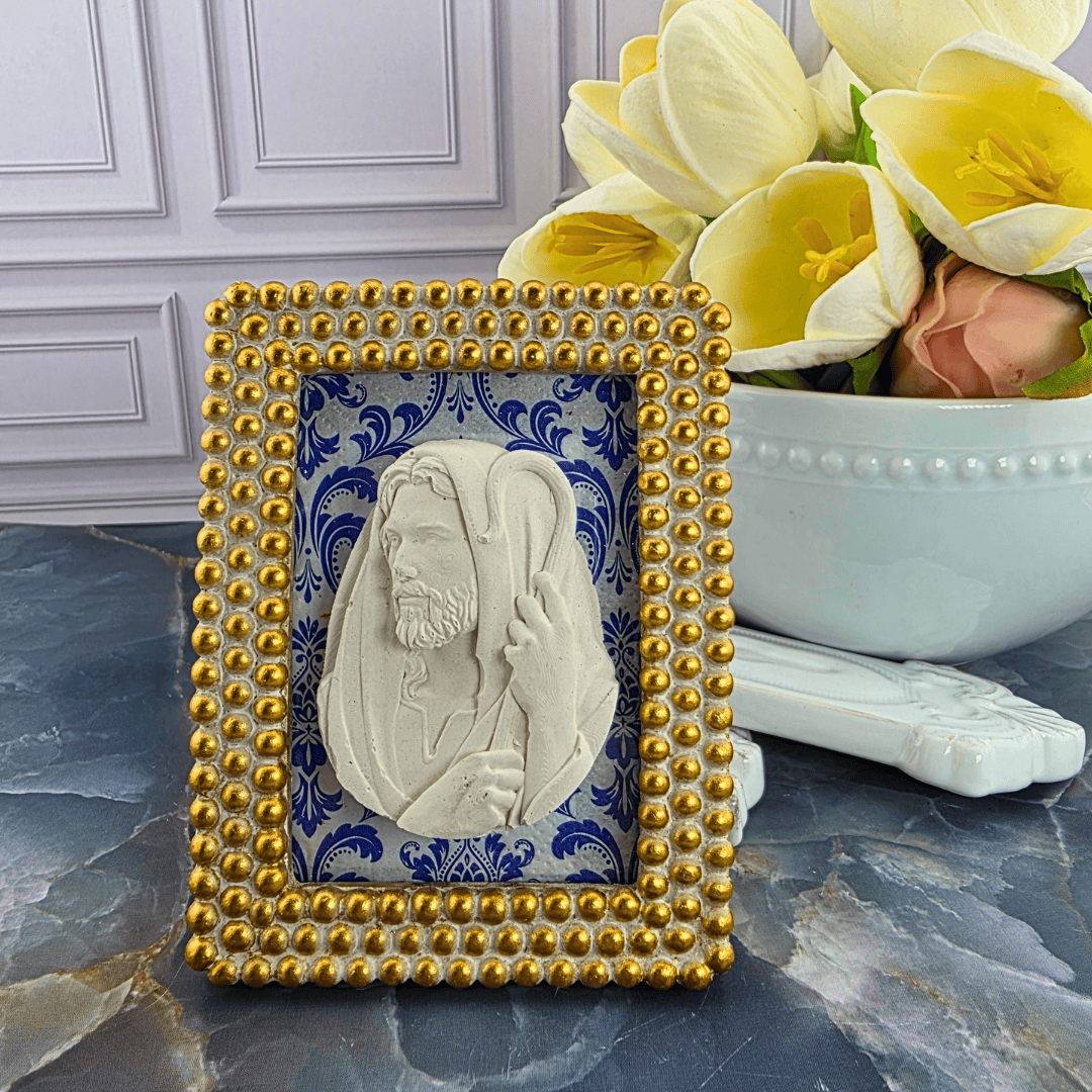 A decorative square frame featuring a carved white portrait of Jesus Christ on a blue patterned background, surrounded by a gold beaded border. Sister Dulce Gift Shop, Shepherds Staff, Religious Store, Cypress Springs Mercedarian Prayer Center, Catholic, 