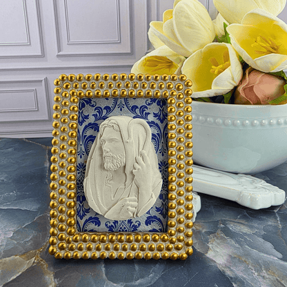 A decorative square frame featuring a carved white portrait of Jesus Christ on a blue patterned background, surrounded by a gold beaded border. Sister Dulce Gift Shop, Shepherds Staff, Religious Store, Cypress Springs Mercedarian Prayer Center, Catholic, 