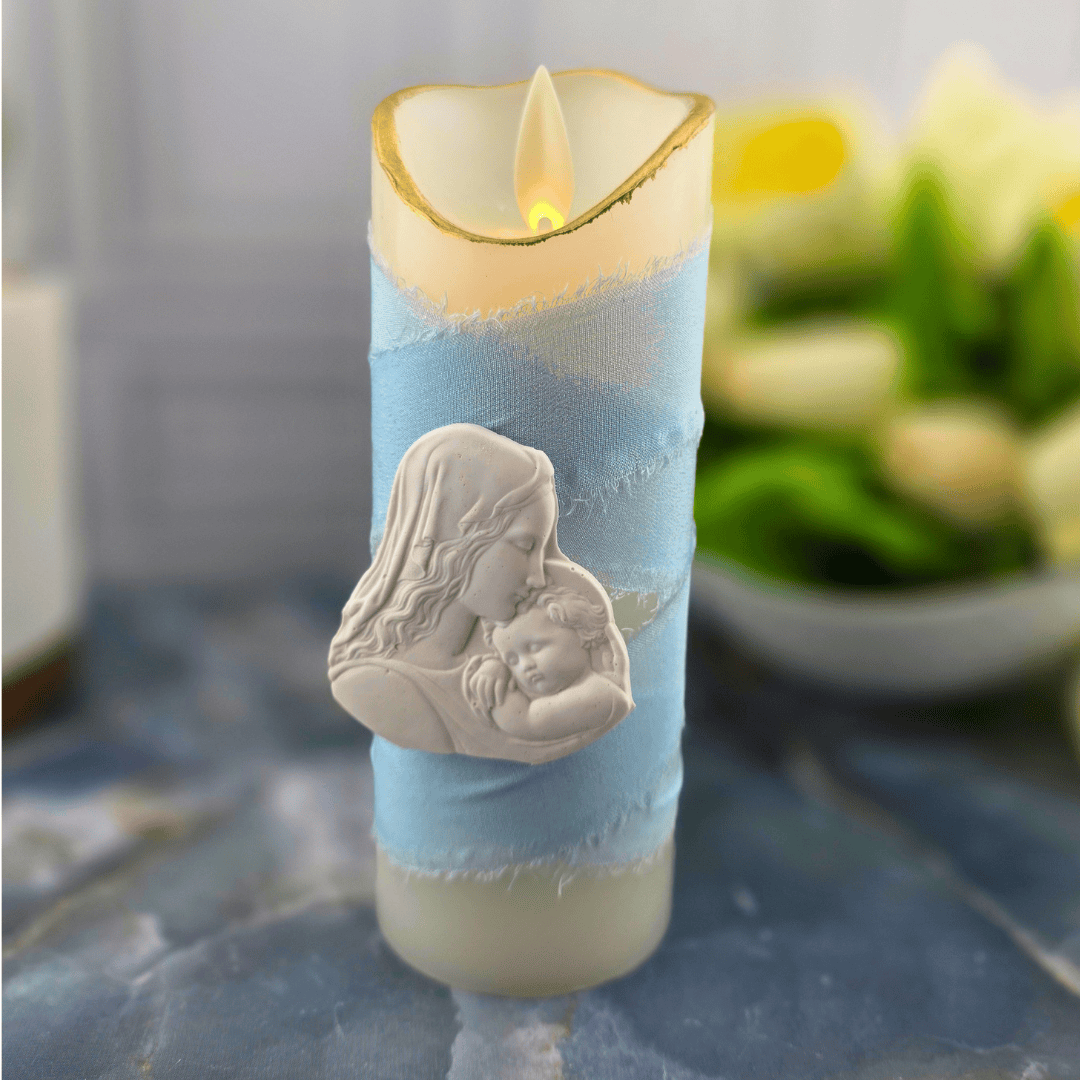 A decorative pillar candle with a light blue fabric wrap and a white relief of a mother and child, flameless candle, light blue madonna and child small, Sister Dulce Gift Shop, Shepherds Staff, Religious Store, Cypress Springs Mercedarian Prayer Center, Catholic, 