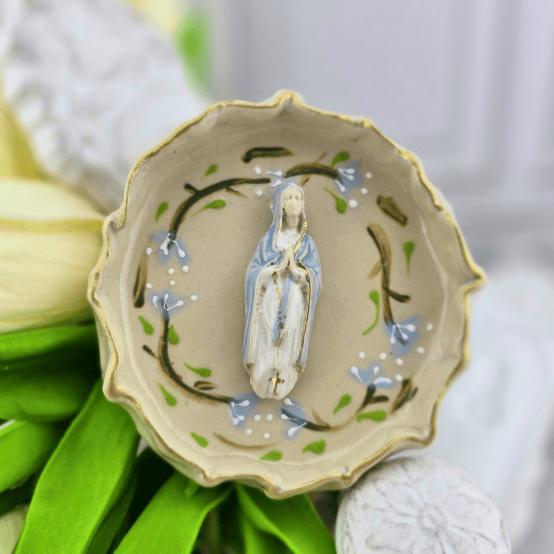 A small ceramic dish with a scalloped rim, featuring a painted figure of the Virgin Mary in the center and delicate blue flowers and green vine motifs around the base, our lady of the rosary, roses, Sister Dulce Gift Shop, Shepherds Staff, Religious Store, Cypress Springs Mercedarian Prayer Center, Catholic, new item, popular item, sacred treasures, trinket dish