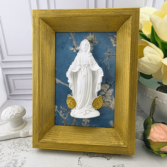 A small framed religious piece featuring a white statue of the Virgin Mary on a textured blue background with gold accents, set in a rustic gold-colored wooden frame. Sister Dulce Gift Shop, Shepherds Staff, Religious Store, Cypress Springs Mercedarian Prayer Center, Catholic, 