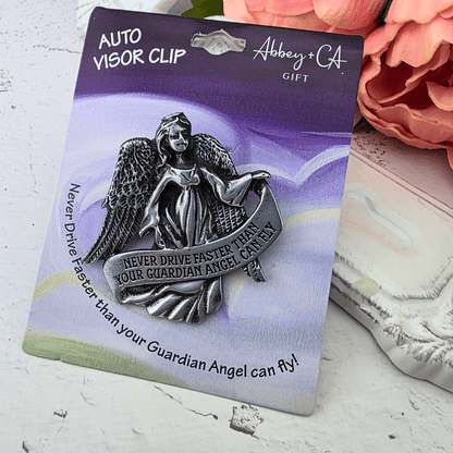A silver-toned guardian angel visor clip mounted on a branded gift card, with the clip featuring an angel holding a banner that says, 'NEVER DRIVE FASTER THAN YOUR GUARDIAN ANGEL CAN FLY!', Sister Dulce Gift Shop, Shepherds Staff, Religious Store, Cypress Springs Mercedarian Prayer Center, Catholic, new item, young adult, new driver