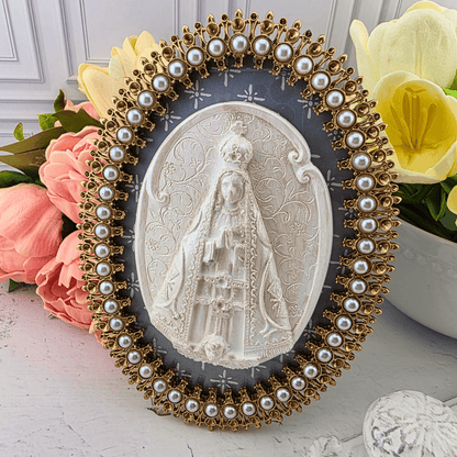 An oval religious plaque featuring a white carved depiction of the Virgin Mary, surrounded by an ornate gold-tone frame adorned with faux pearls, Sister Dulce Gift Shop, Shepherds Staff, Religious Store, Cypress Springs Mercedarian Prayer Center, Catholic, new item, popular item, home decor